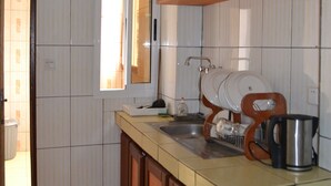 Une cuisine avec des murs recouverts de carreaux blancs, des armoires en bois, une fenêtre et un fourneau.