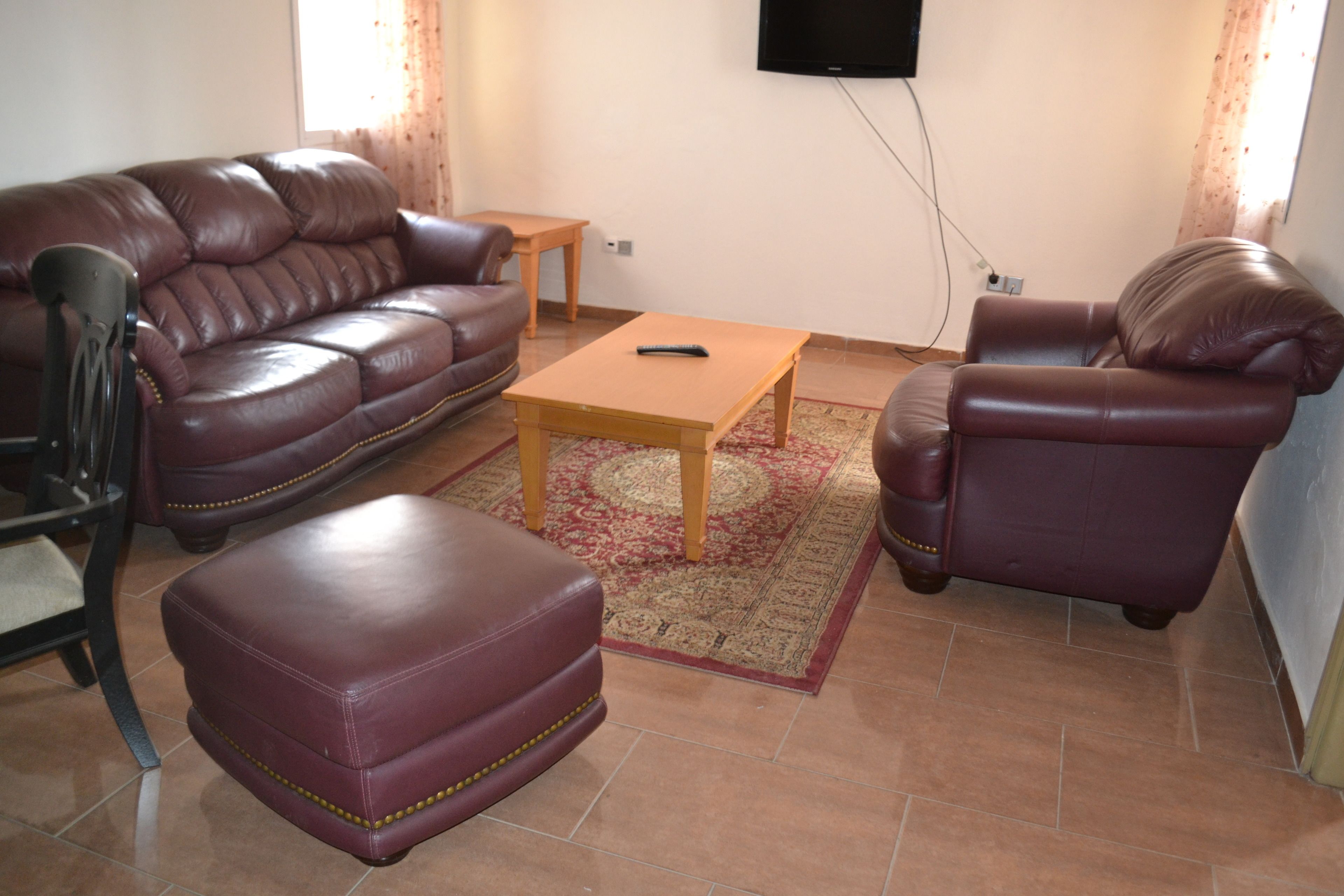 A living room with a brown leather sofa, a matching armchair, a wooden coffee table, and a television mounted on the wall.