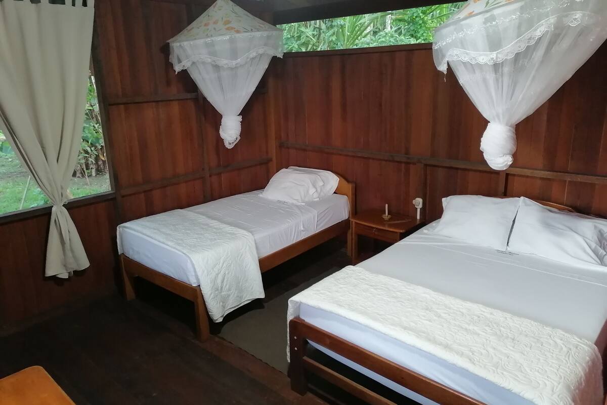 Una habitación con dos camas de madera, cada una con ropa blanca y un mosquitero encima.