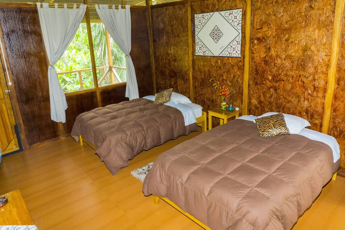 Una habitación con dos camas, paredes de madera y una ventana con cortinas.
