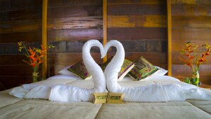 A bed with a heart-shaped towel arrangement and two pillows with colorful patterns. - Amazon Planet (Tambopata)