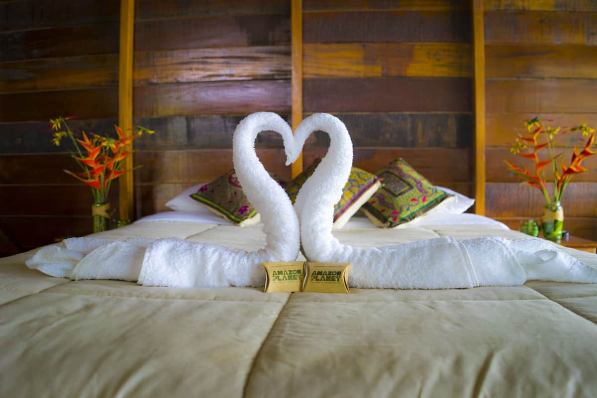 Una cama con una toalla dispuesta en forma de corazón y dos almohadas con diseños coloridos.