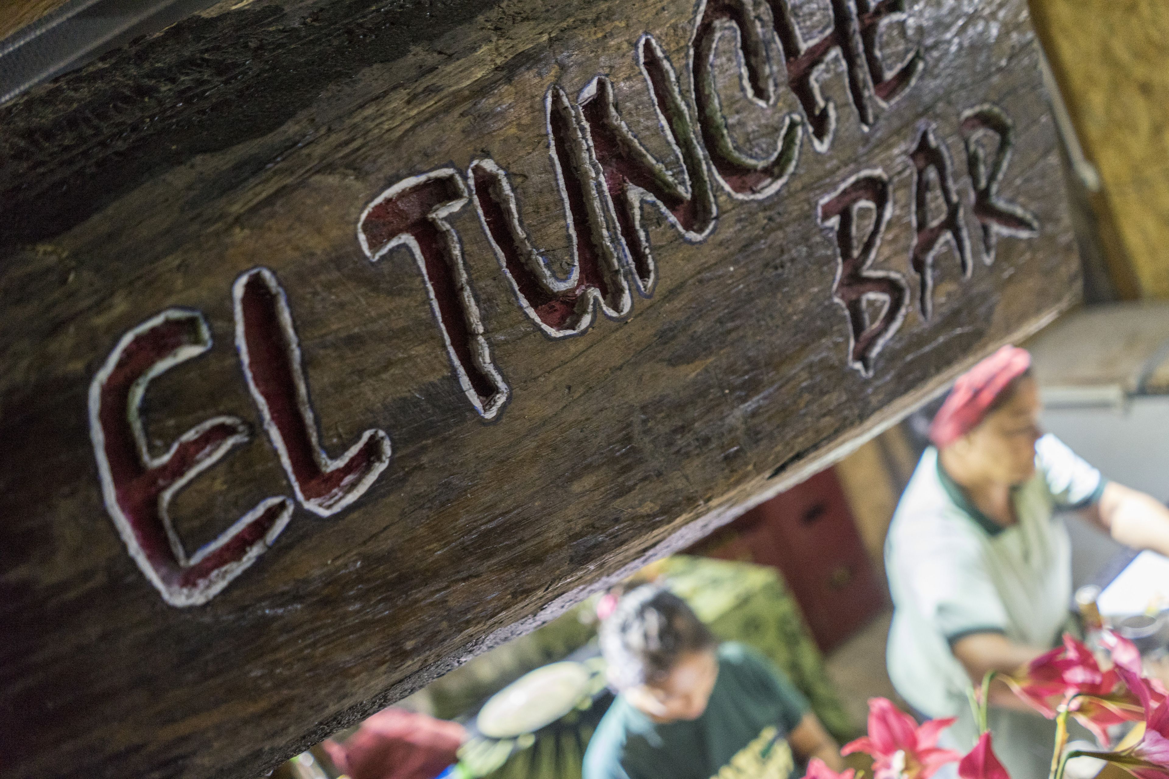 A wooden sign with the text "EL TUNCHE BAR" indicating a bar establishment.