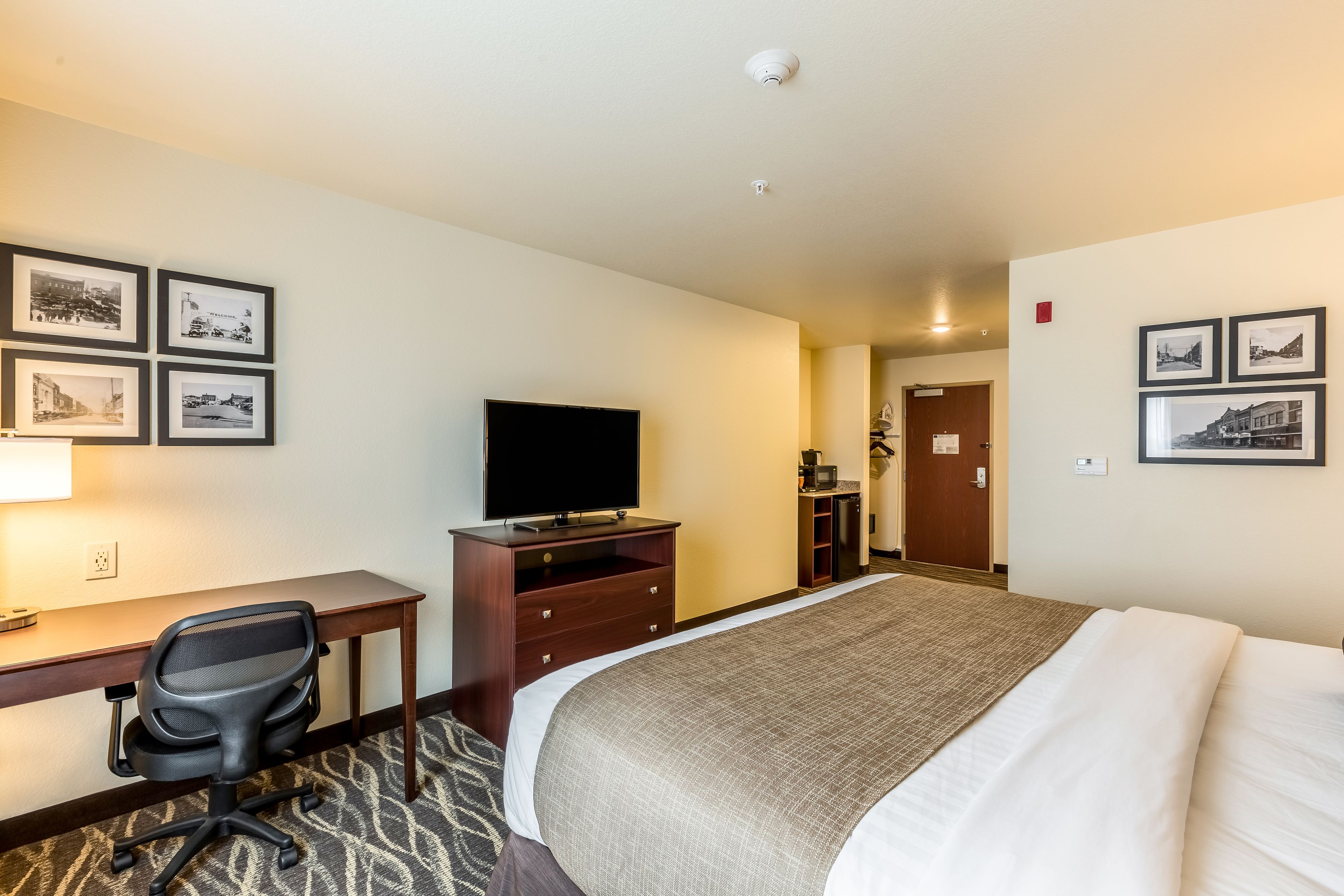 A hotel room with a bed, desk, chair, television, and framed pictures on the walls.