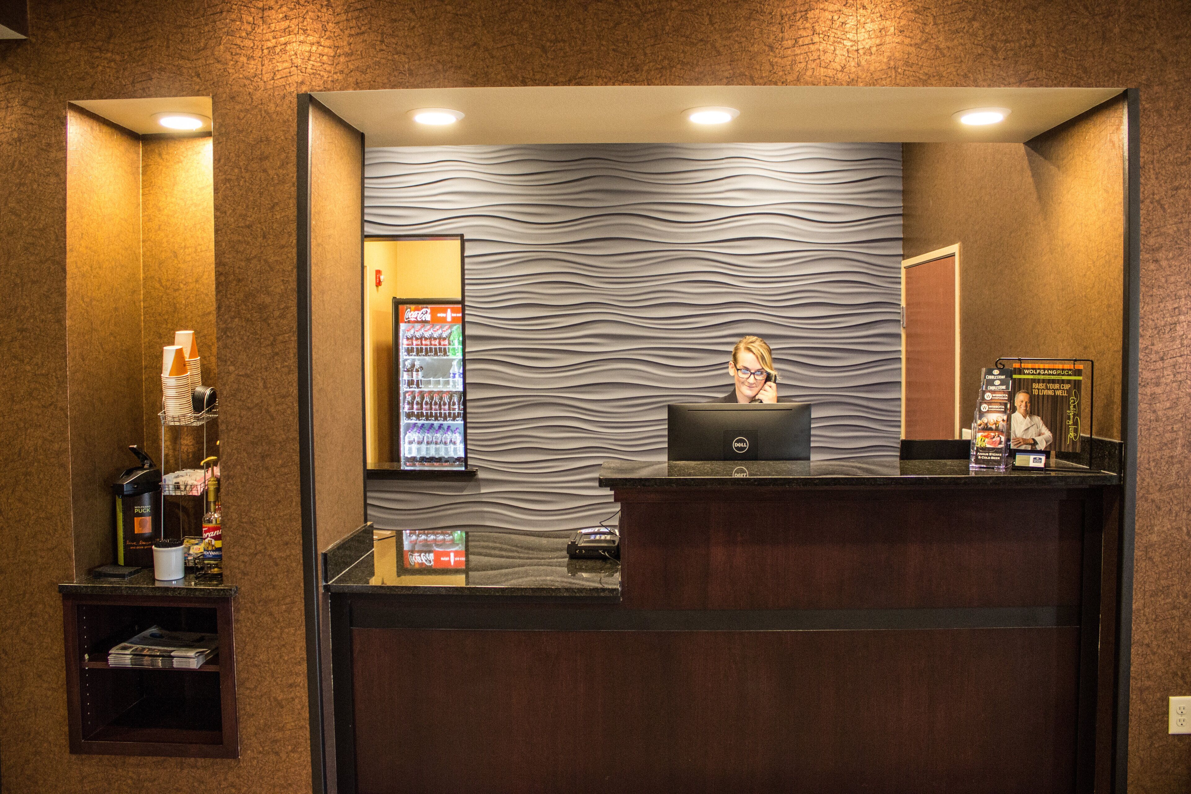 A reception desk with a laptop, a Coca-Cola refrigerator, and a vending machine.