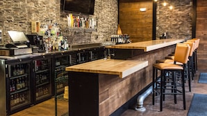 Un espace bar doté d’un long comptoir, de tabourets et de diverses bouteilles exposées sur des étagères.