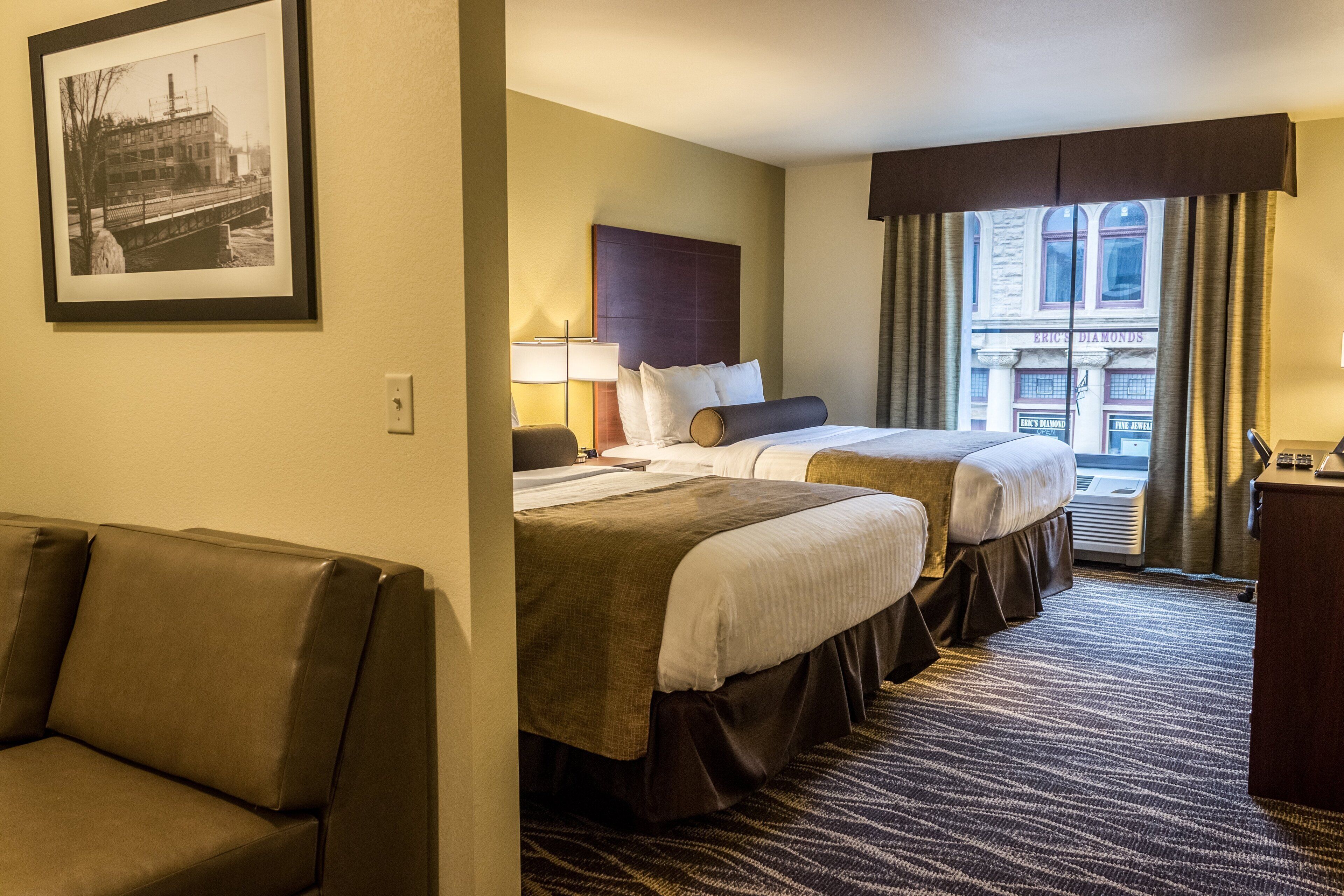 A hotel room with two beds, a sofa, a desk, and a window with a view of a building.