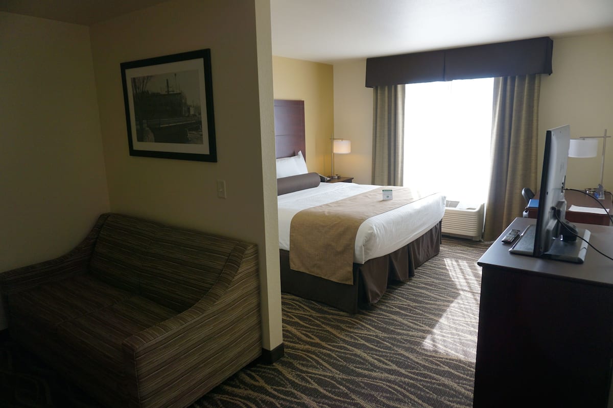 Ein Hotelzimmer mit Bett, Sofa, Schreibtisch mit Computer und Fenster mit Vorhängen.