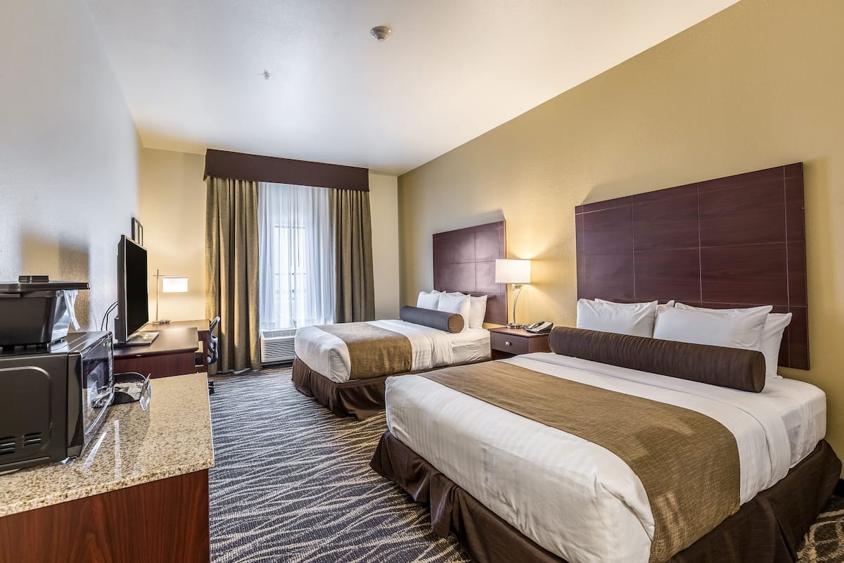 Ein Hotelzimmer mit zwei Betten, einem Schreibtisch mit Fernseher und einem Fenster mit Vorhängen.