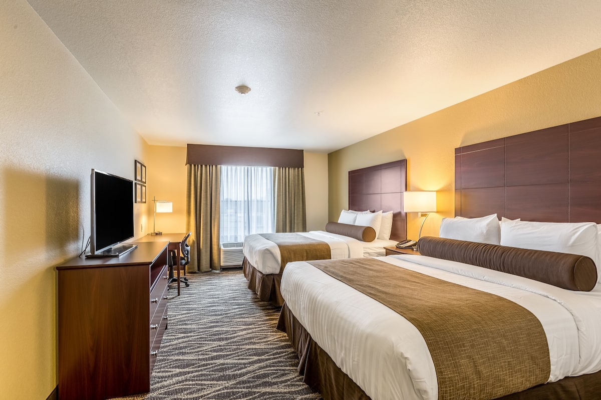 Ein Hotelzimmer mit zwei Betten, einem Schreibtisch, einem Fernseher und einem Vorhangfenster.