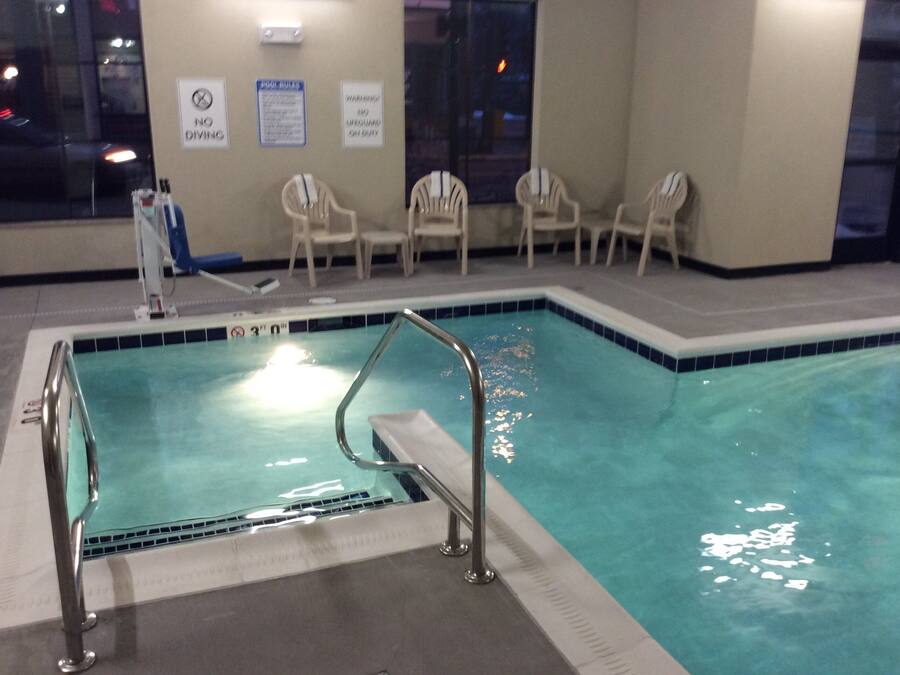 Piscina interior com escada de metal, cadeiras e placas com as regras da piscina na parede.
