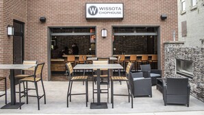 Un espace extérieur aménagé avec des tables et des chaises, un bâtiment en briques sur lequel on peut lire l’inscription « Wissota Chophouse », et un mur de pierre avec un téléviseur.