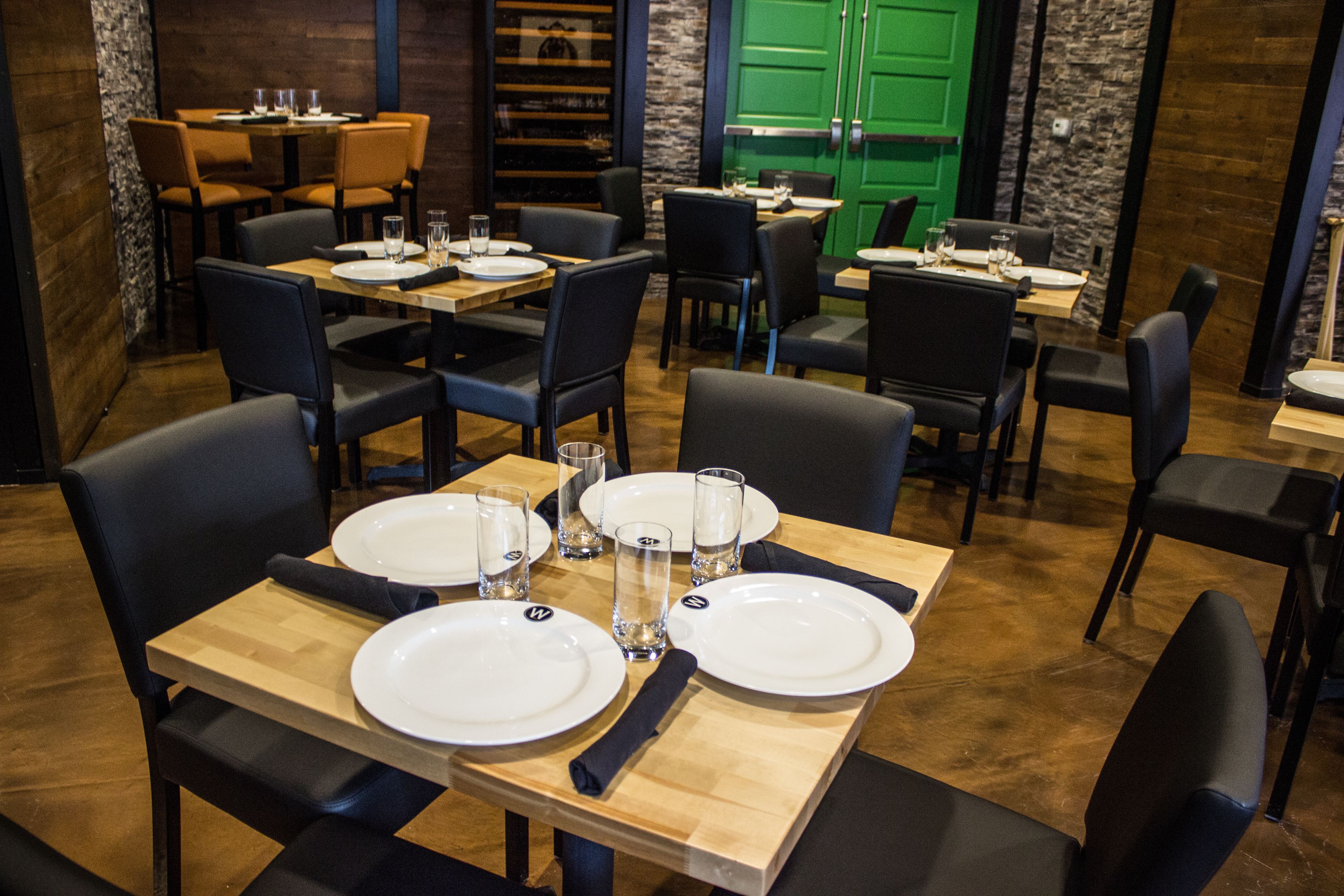 A restaurant with multiple tables set for dining, featuring black chairs and wooden tables.