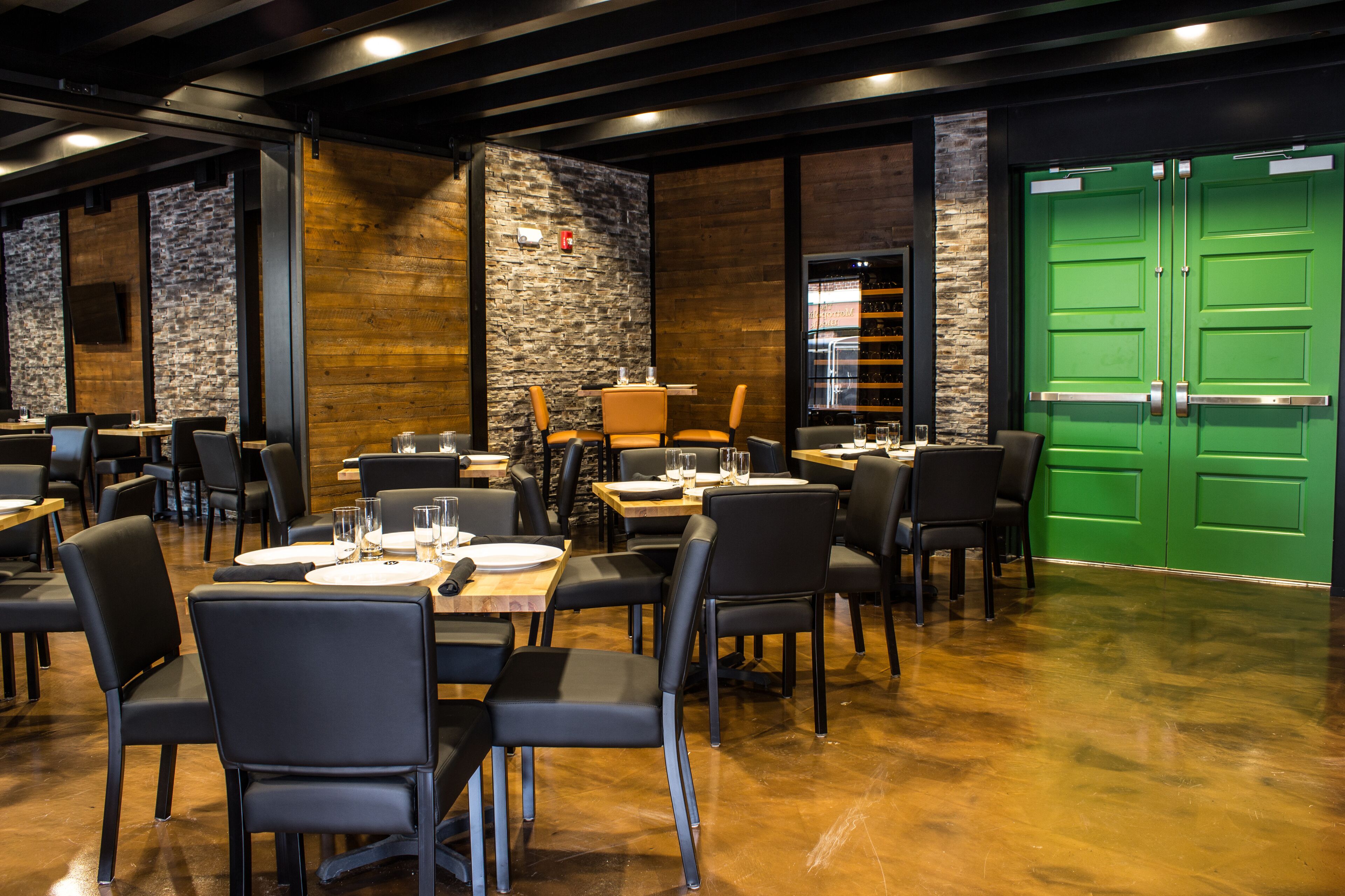 Un ristorante con diversi tavoli e sedie, una porta verde e un muro in pietra.