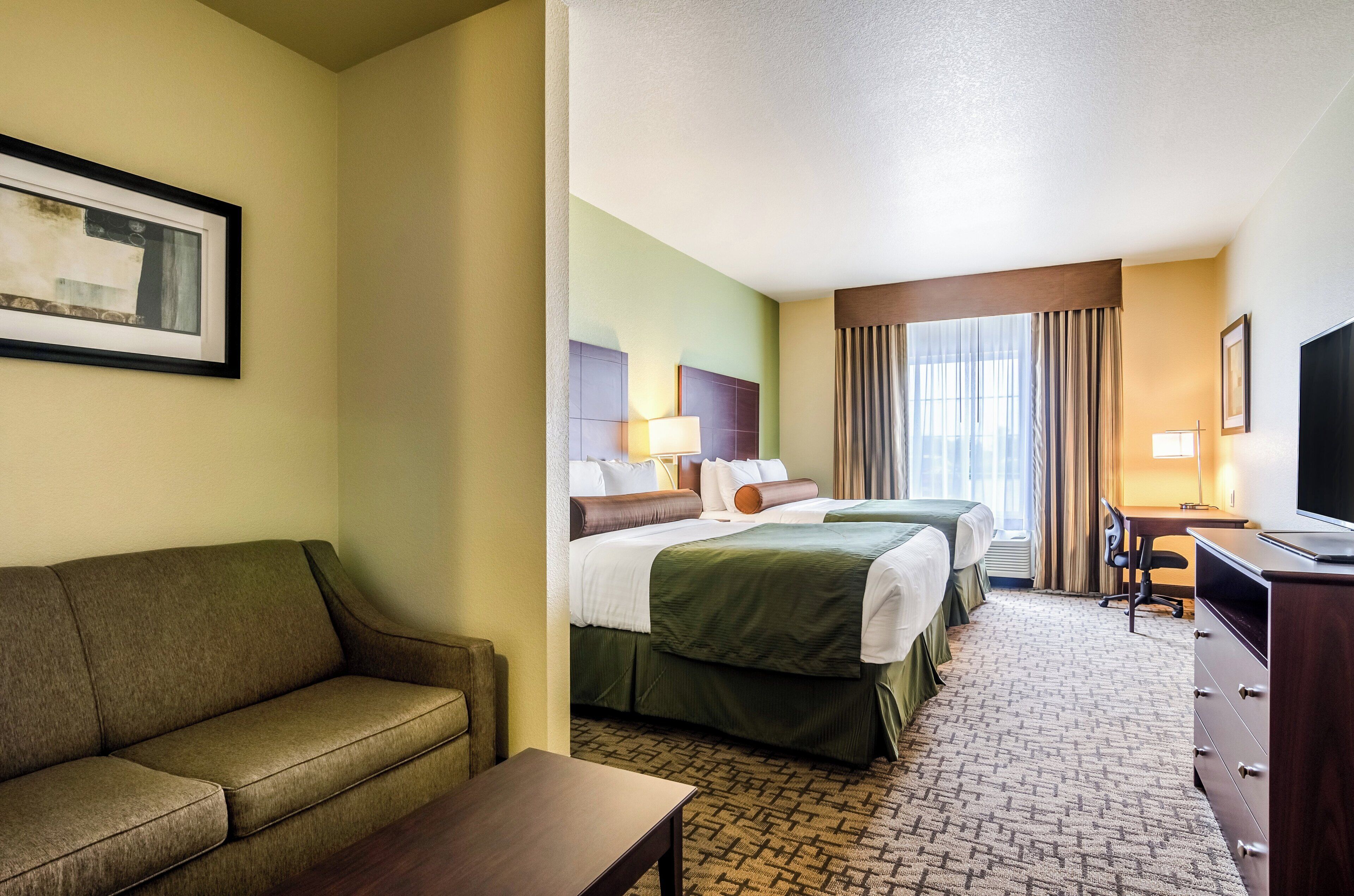 A hotel room with a sofa, two beds, a desk, and a TV.