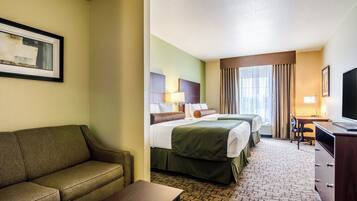 A hotel room with a sofa, two beds, a desk, and a TV.