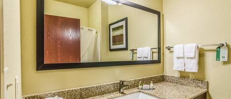 A bathroom with a granite countertop, a white sink, a mirror, and a towel rack.