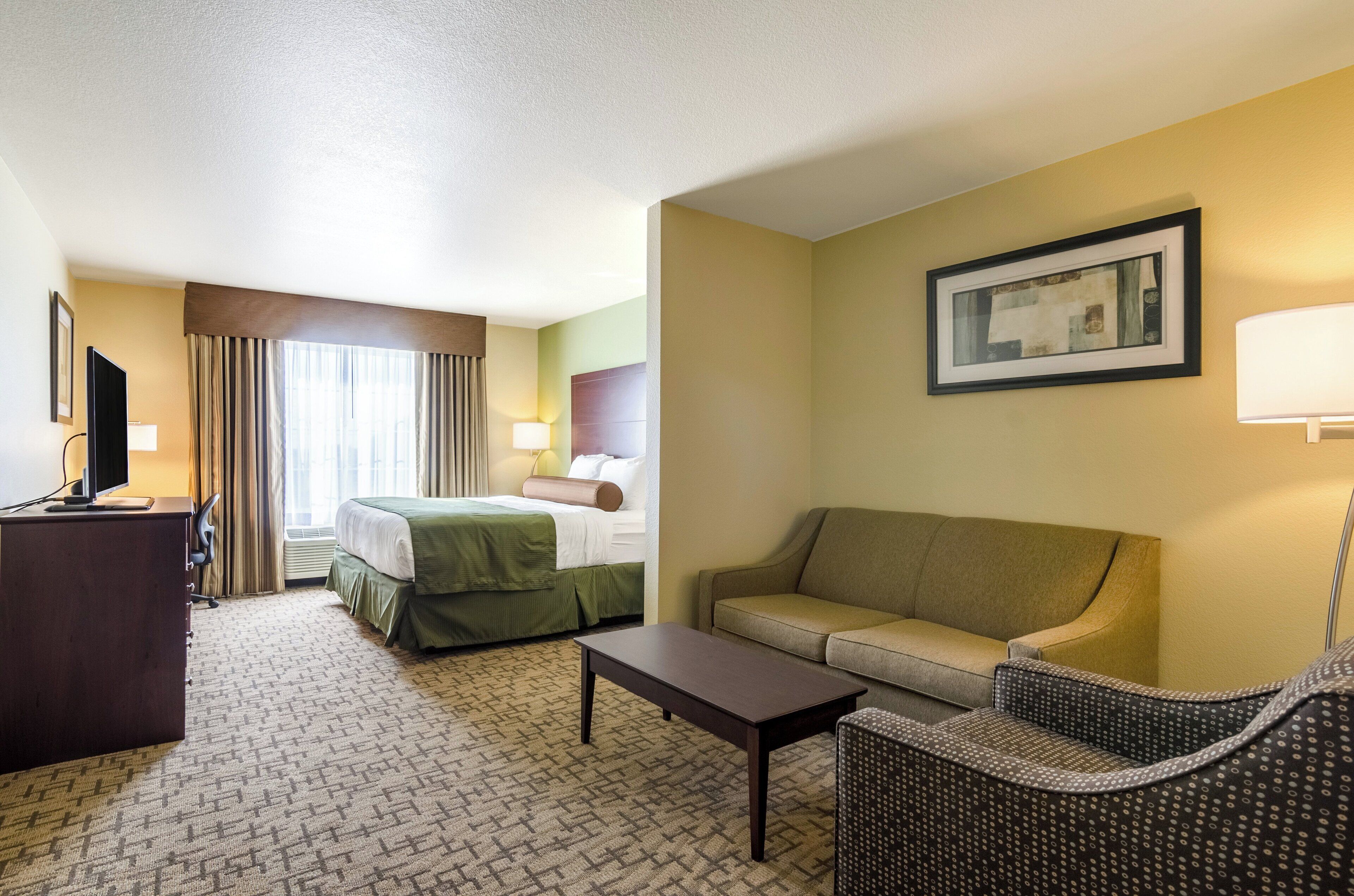 Una habitación de hotel con una cama, un sofá, una mesa de centro y un escritorio con una lámpara.