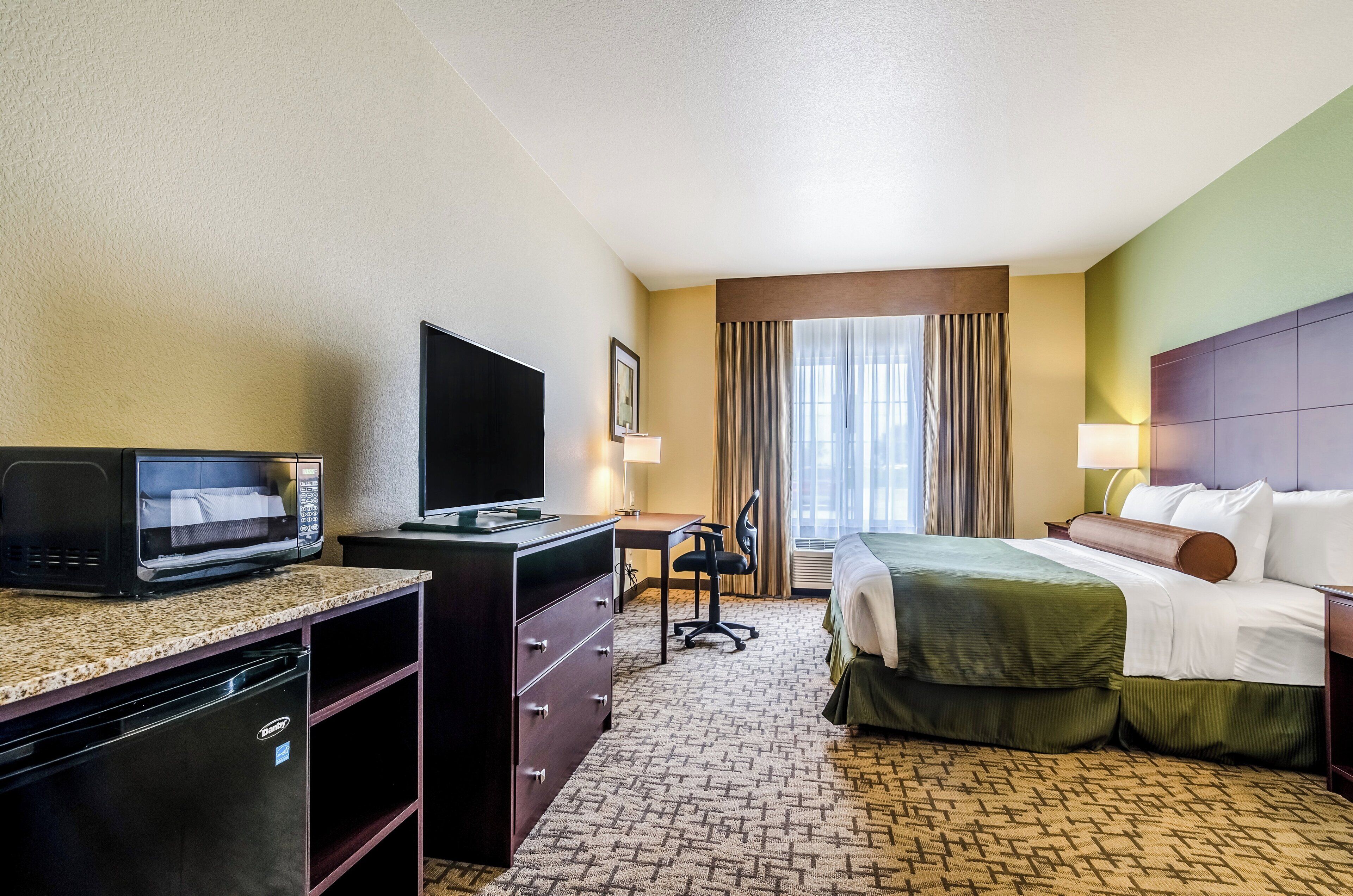 A hotel room with a bed, desk, microwave, and a television.