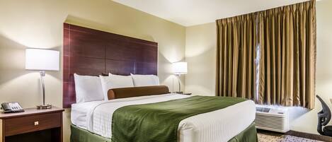 Habitación de hotel con cama, dos lámparas de noche, teléfono, unidad de aire acondicionado y ventana con cortinas.