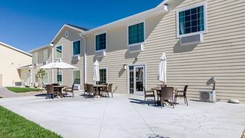 A residential building with multiple windows, outdoor seating areas with umbrellas, and air conditioning units.