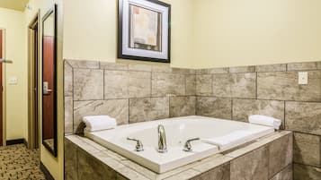 A bathroom with a large bathtub, a framed picture on the wall, and a tiled floor.