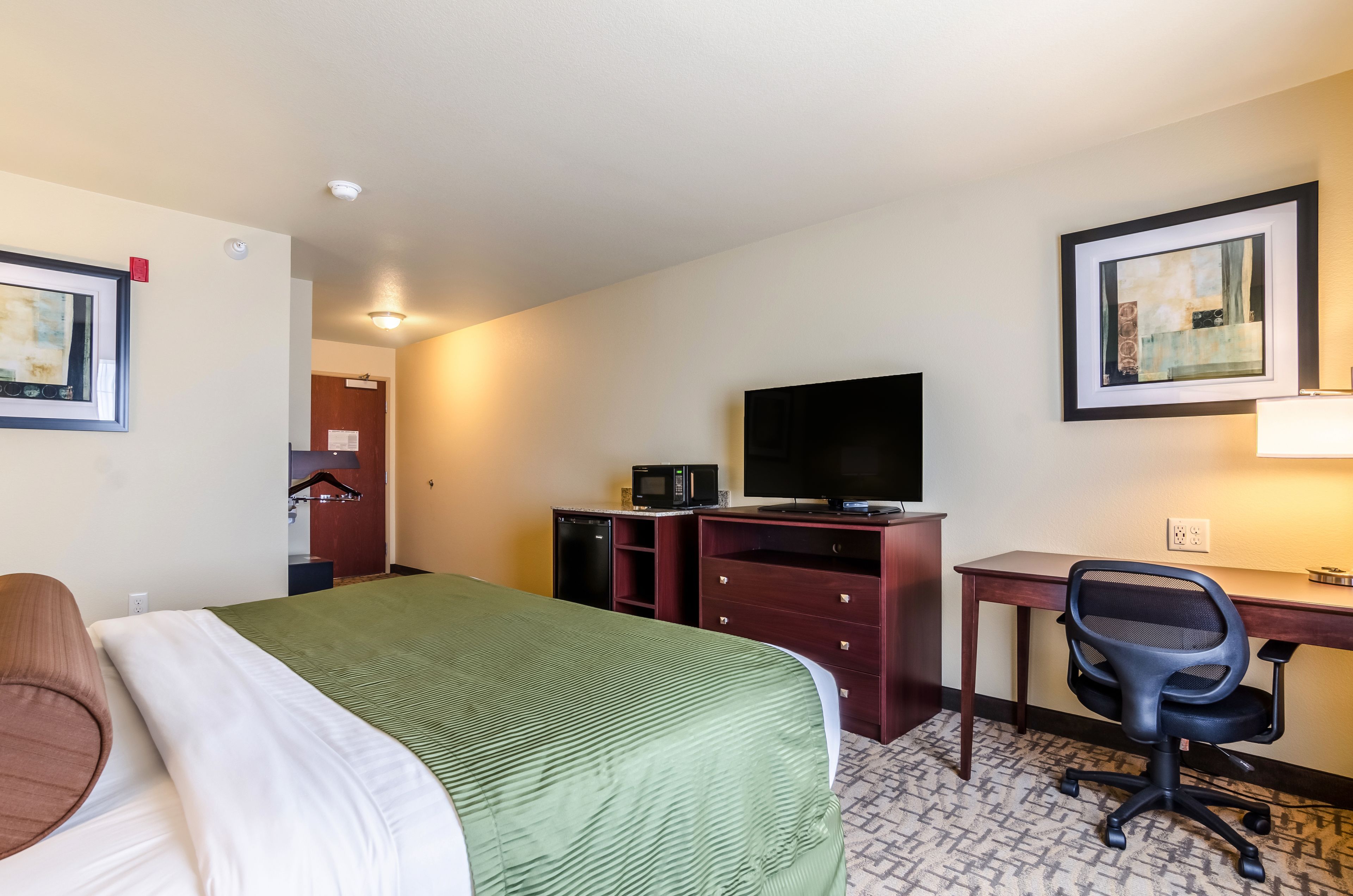 A hotel room with a bed, desk, chair, television, and a microwave.