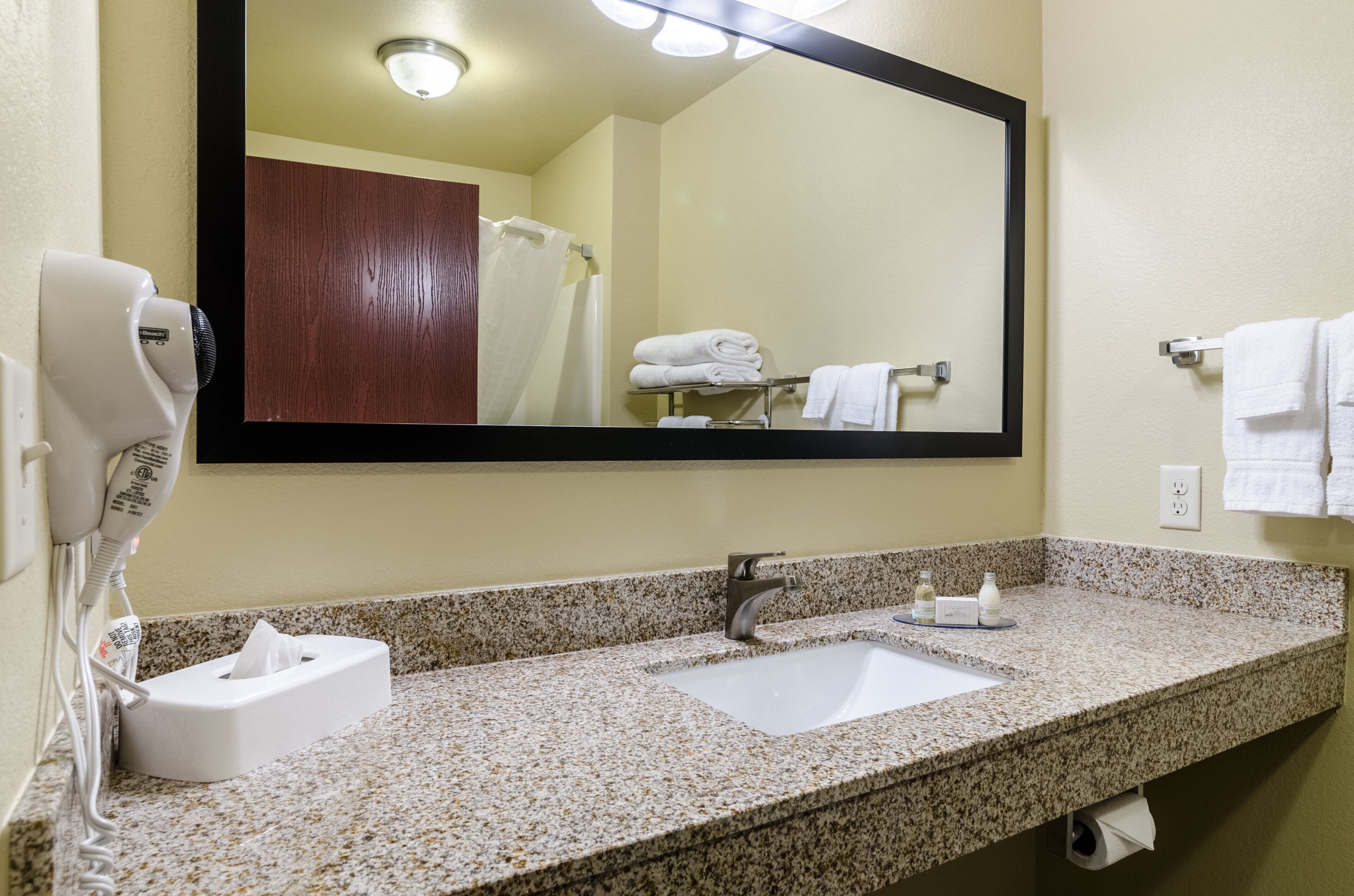 A bathroom with a granite countertop, a white sink, a mirror, a towel rack, and a hairdryer.