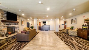 A spacious lobby with a stone fireplace, comfortable seating, a reception desk, and a patterned carpet.
