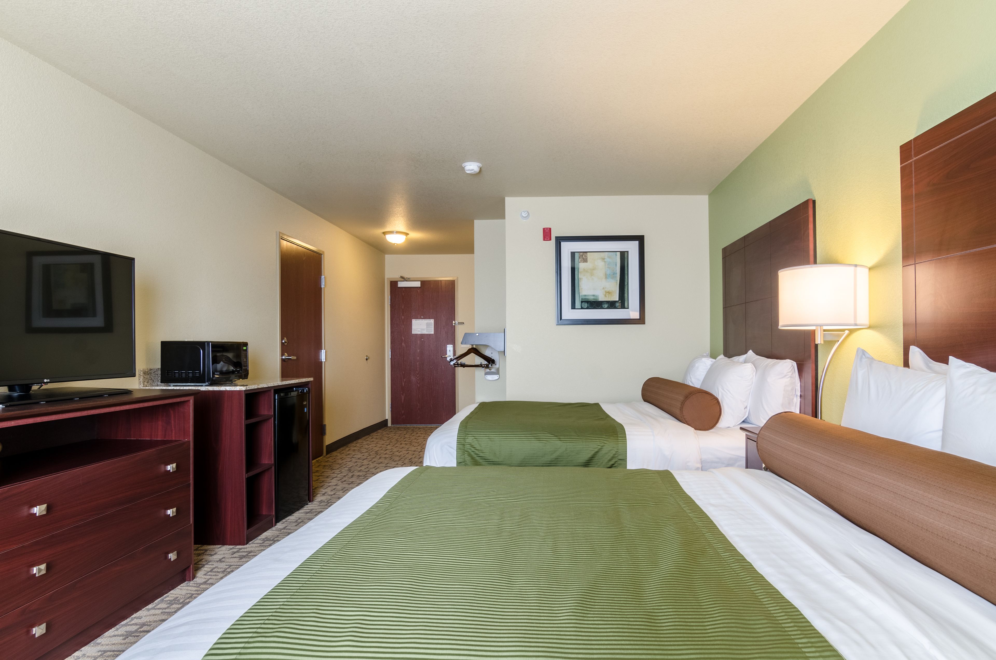 A hotel room with a bed, a desk with a television, a microwave, and a coat rack.
