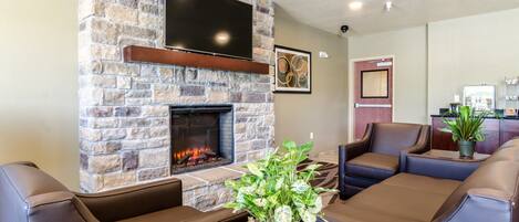 A stone fireplace with a flat-screen TV above it, leather sofas, and a potted plant on a wooden table.