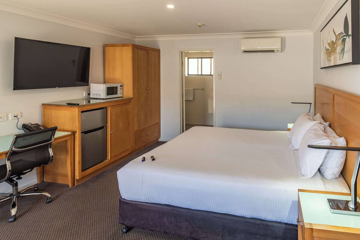 Ein Hotelzimmer mit einem Bett, einem Schreibtisch mit Computer, einer Mikrowelle und einem Fernseher.