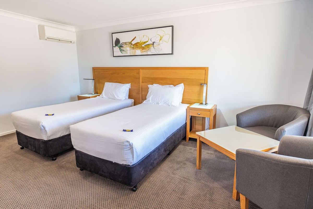 Ein Hotelzimmer mit zwei Einzelbetten, einem Holzkopfteil, einem Schreibtisch und einem Stuhl.