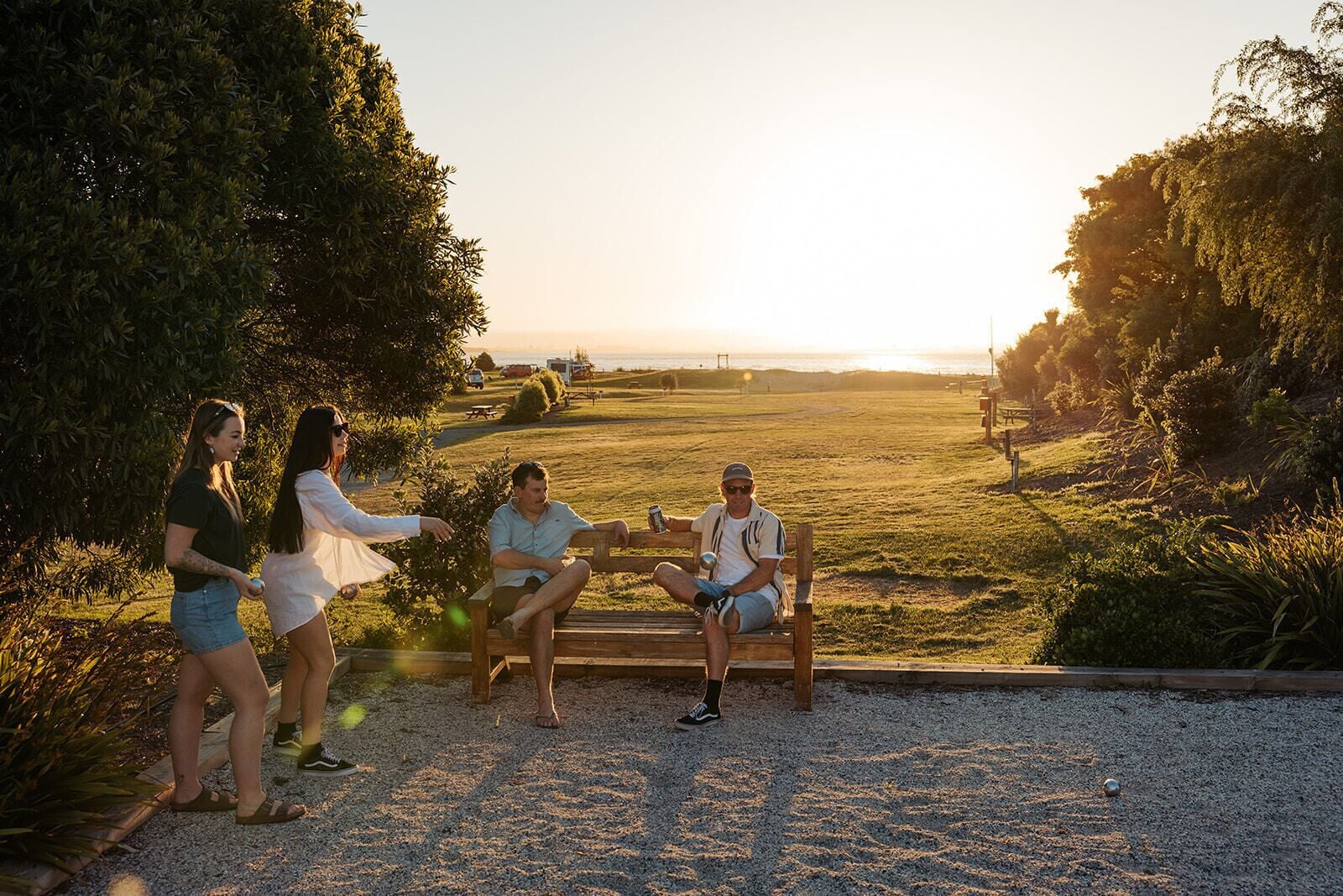 A group of people sitting on a bench in a park with a view of the sunset.