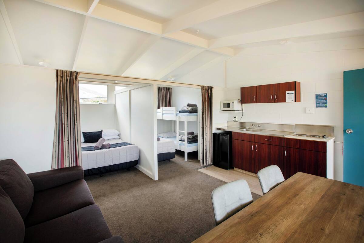 A compact room with bunk beds, a kitchenette, a dining table, and a sofa.
