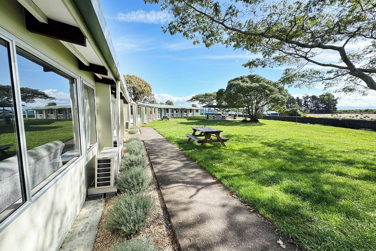 A row of motel rooms with a grassy lawn and picnic table.