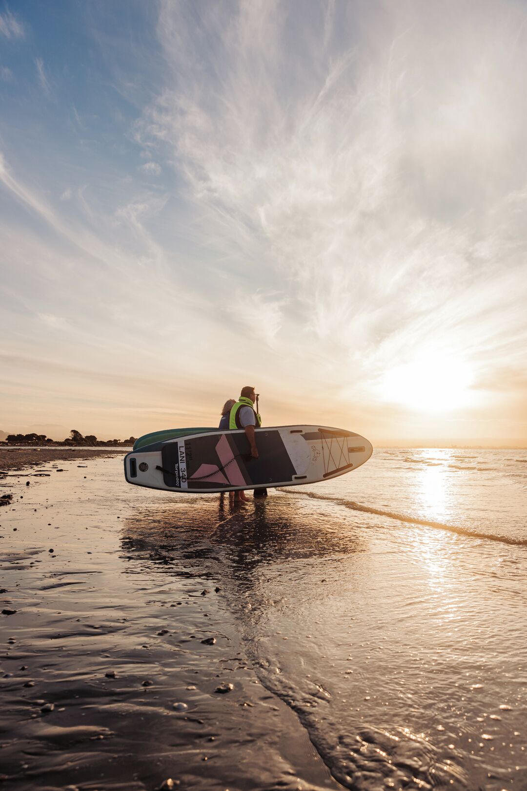 Eine Person trägt ein Stand-Up-Paddleboard am Strand bei Sonnenuntergang.