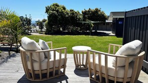 A wooden deck with two beige armchairs and a small round table, overlooking a grassy yard and a building with a sign that reads "GALLERY". - Tahuna Beach Holiday Park  (Nelson)
