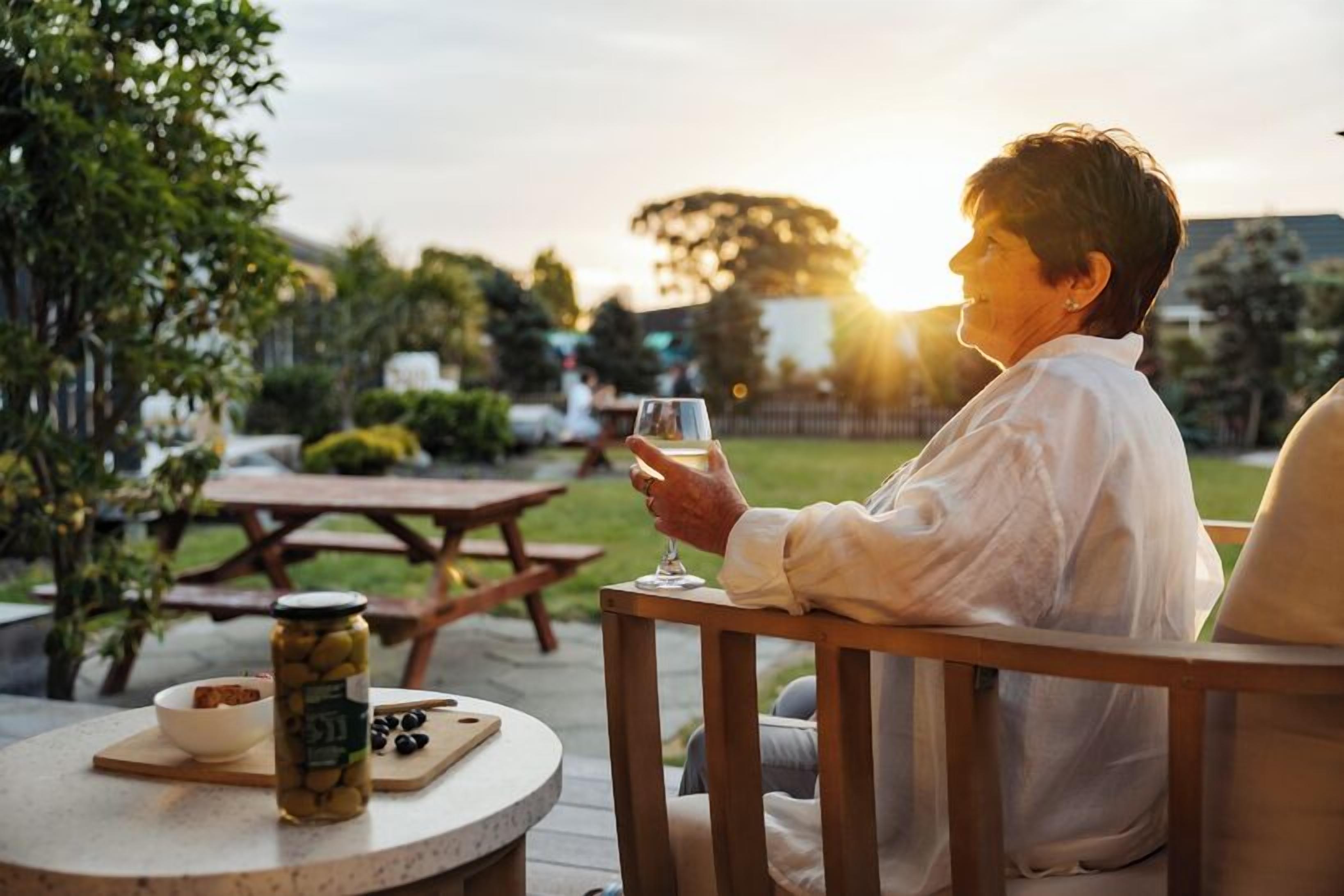 An outdoor patio area with a round table, a picnic table, and a person seated at the table holding a glass.
