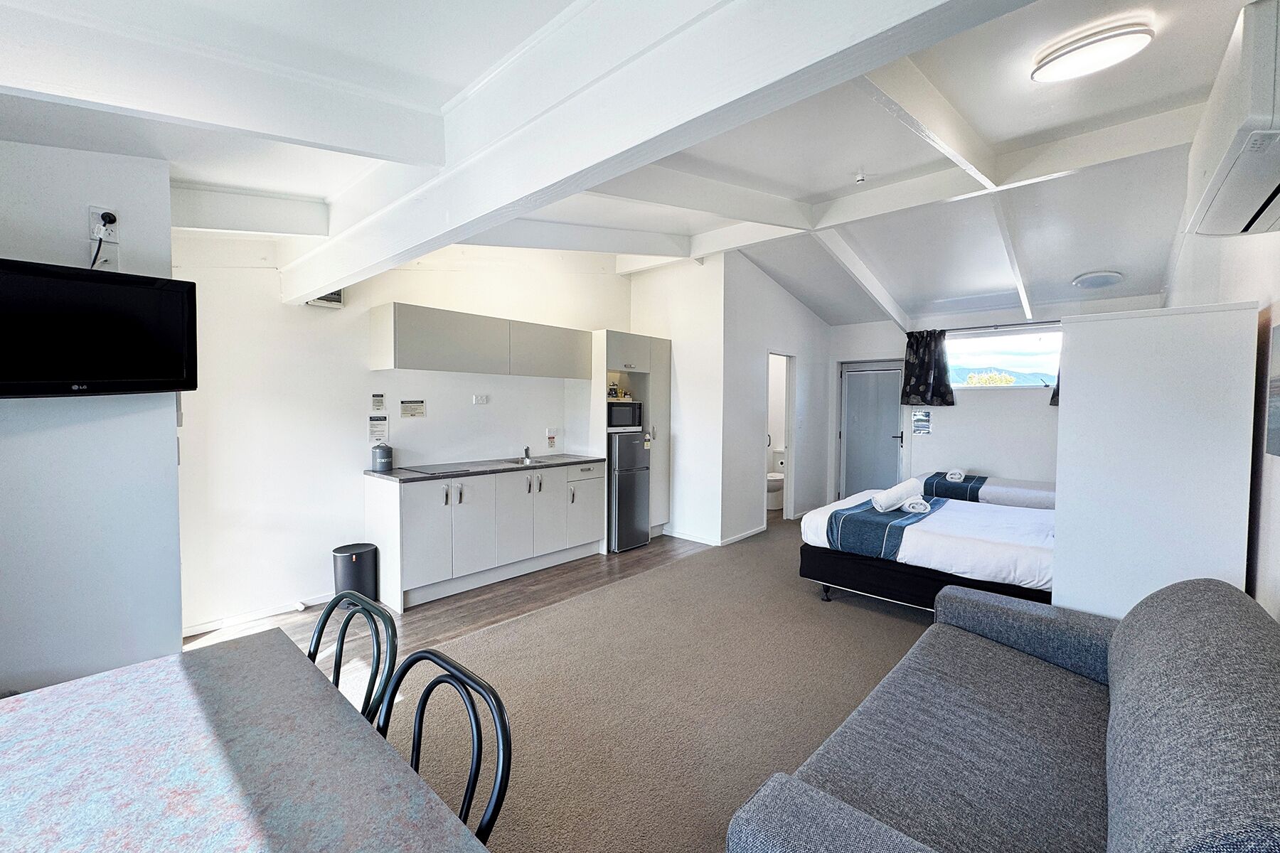 A compact living space with a kitchenette, a sofa, a bed, and a television.
