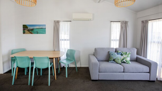 A room with a grey sofa, teal chairs, a wooden table, and two pendant lights. - Tahuna Beach Holiday Park  (Nelson)