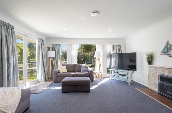 A modern living room with a sofa, ottoman, and a glass coffee table. There is a television and a fireplace.