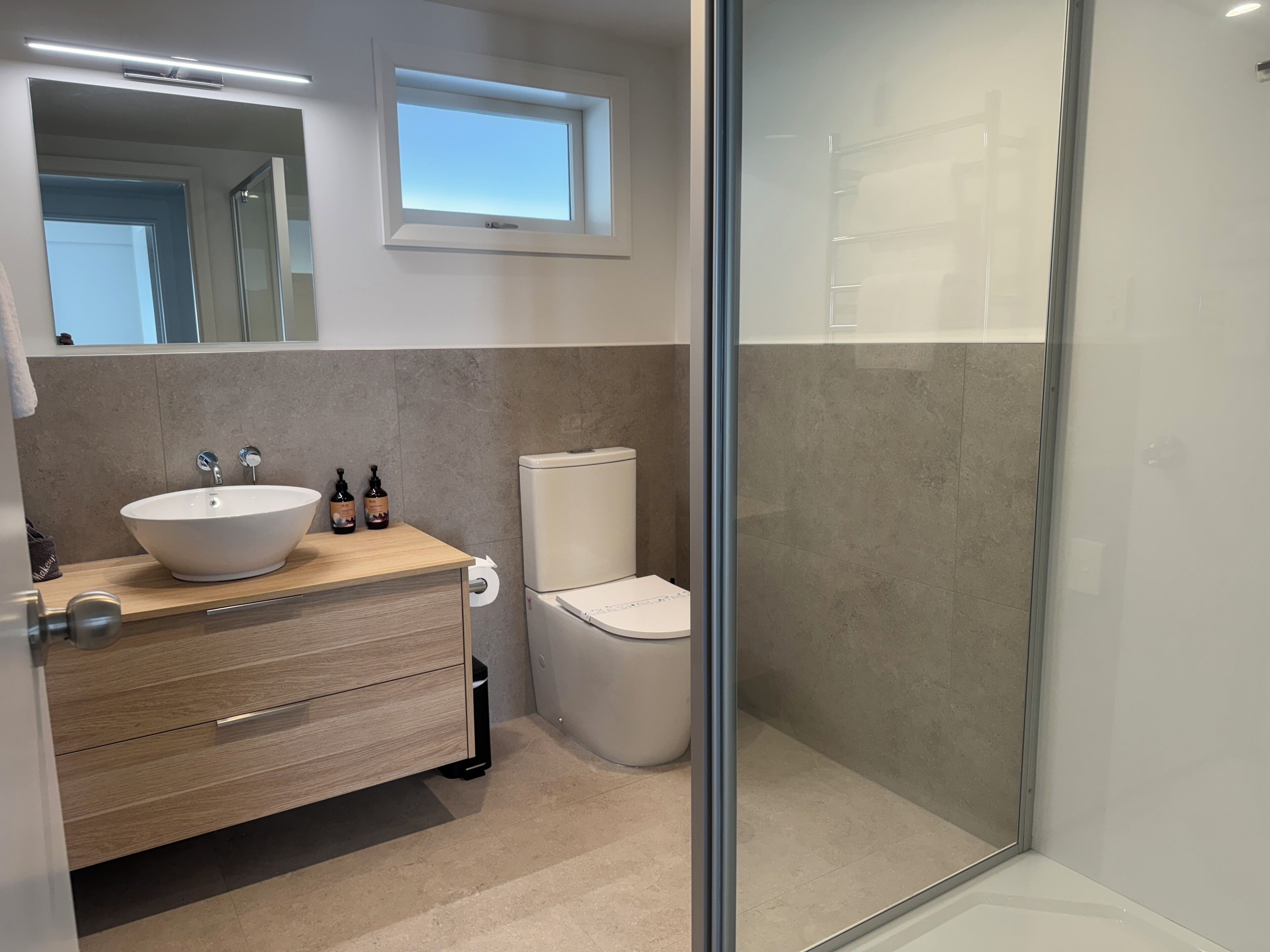 Ein modernes Badezimmer mit einem Holzkosmetikschrank, einem weißen Waschbecken und einer Toilette.