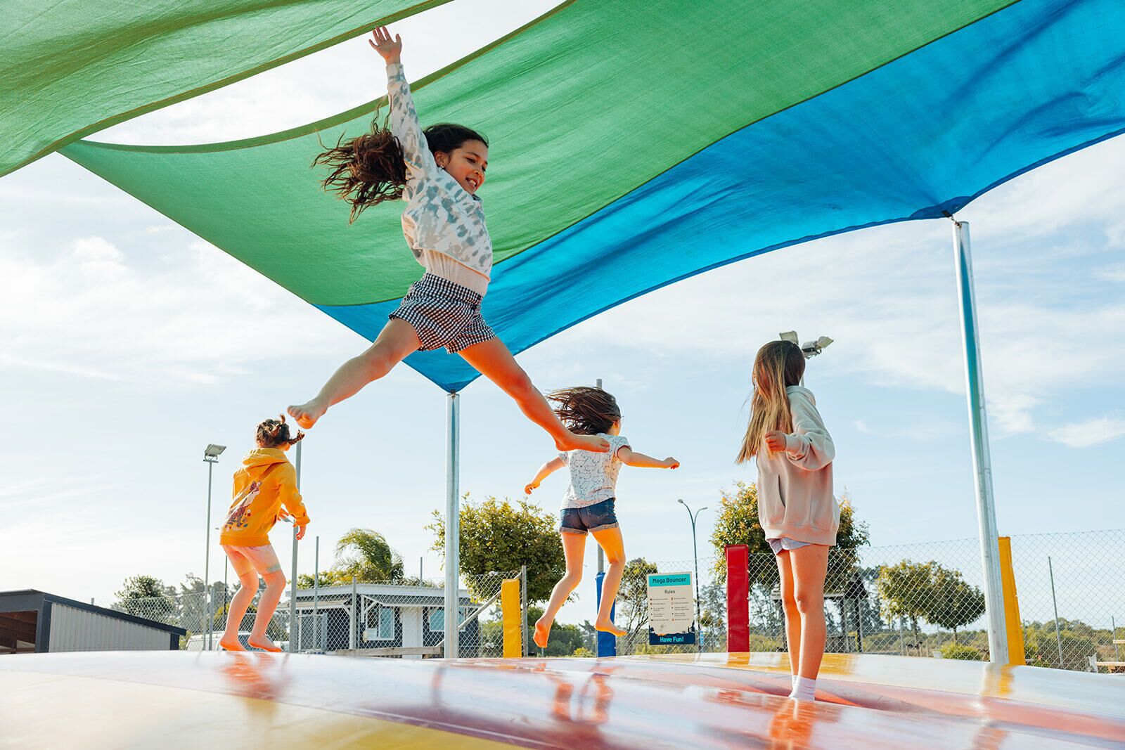 Children playing on a trampoline under a canopy.