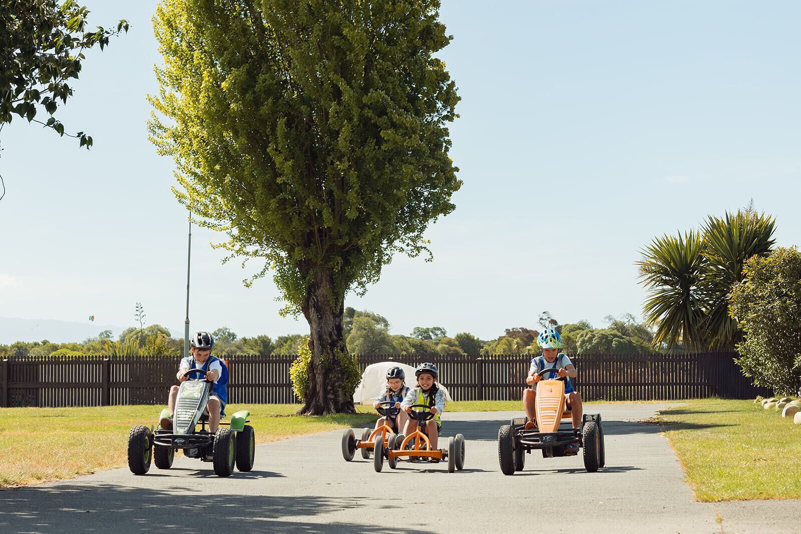 Three children riding go-karts on a paved path.