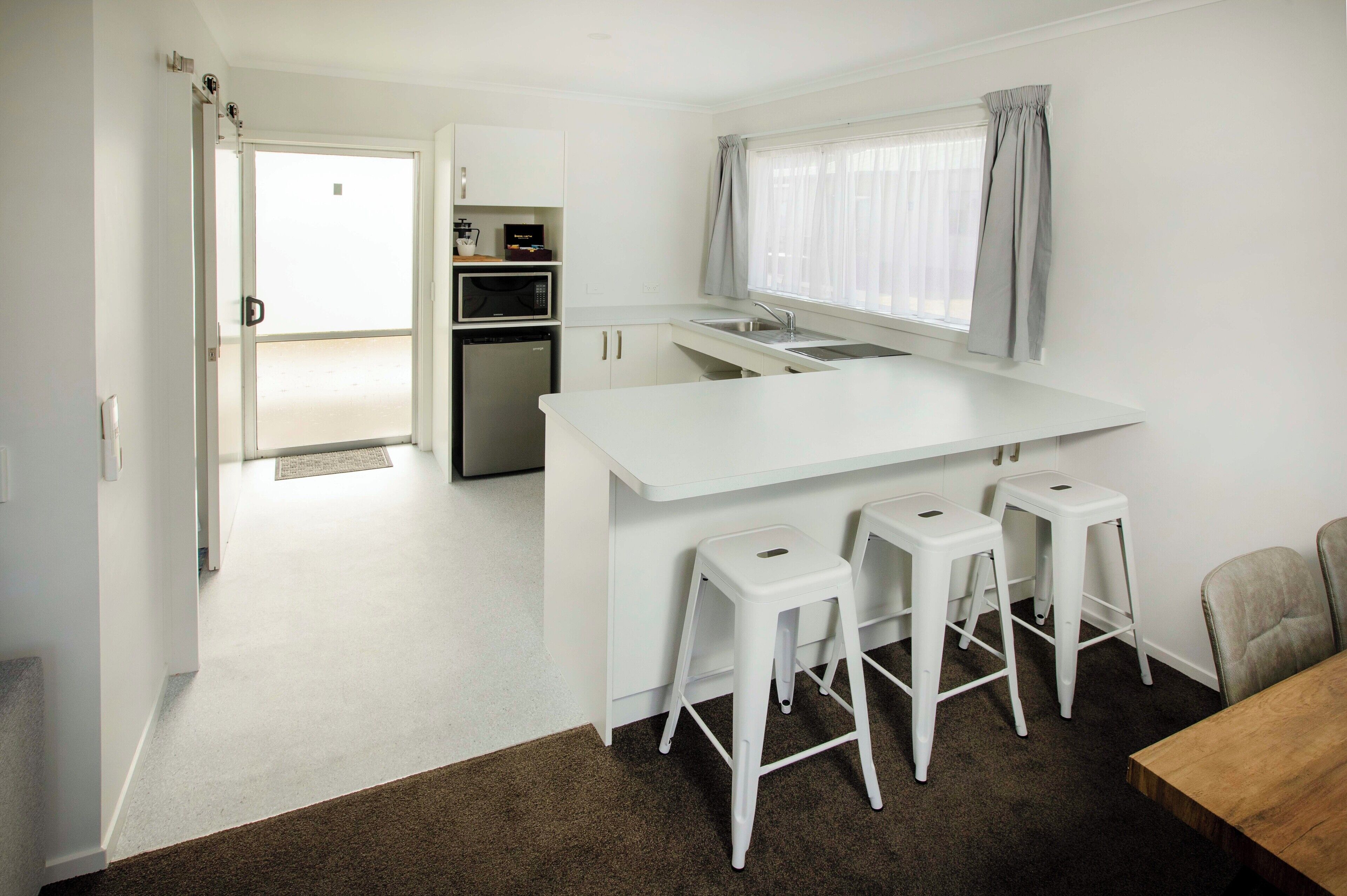 A compact kitchen with white cabinetry, a built-in microwave, and a window with curtains.