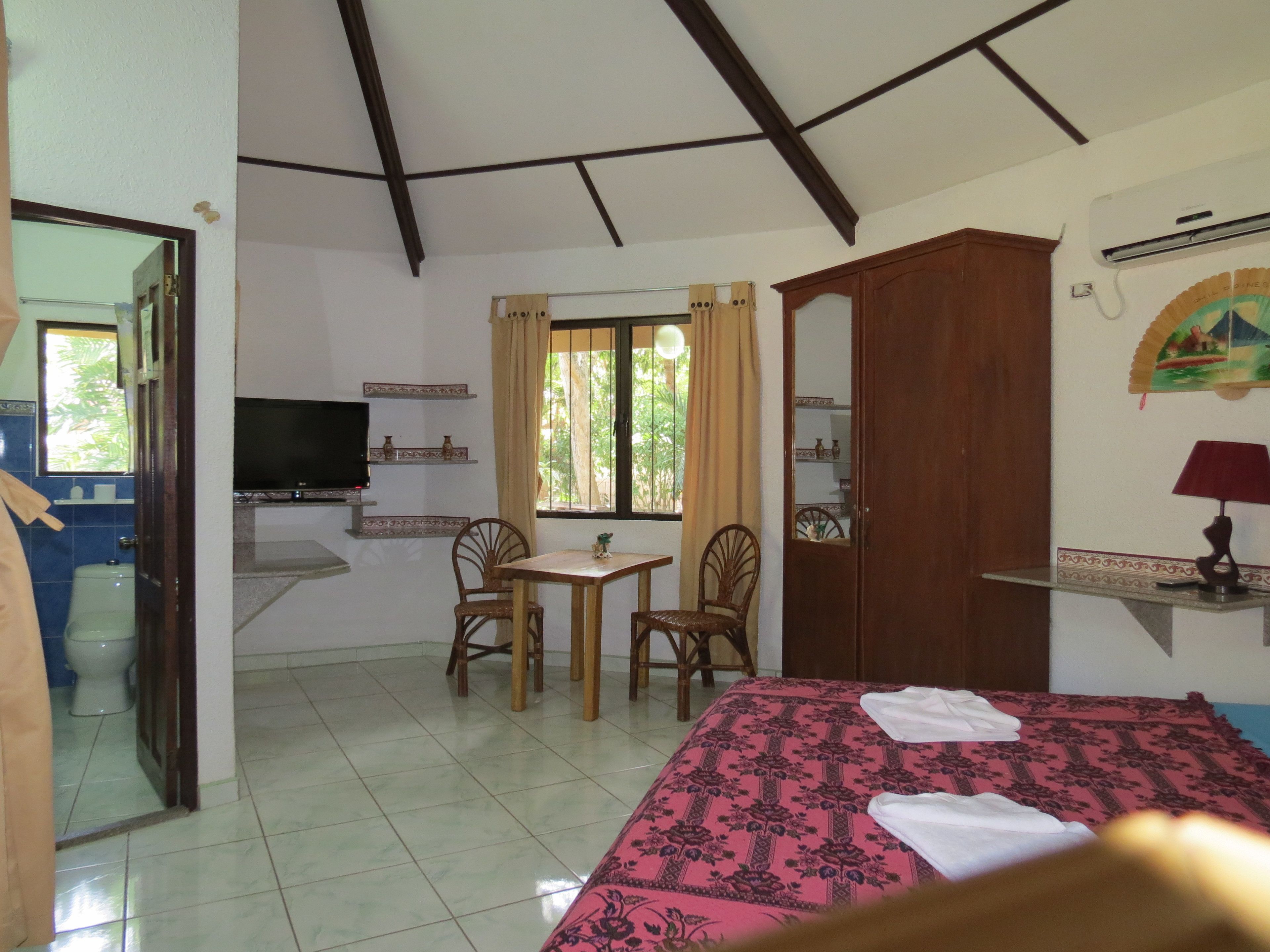 Una habitación con cama, televisión, mesa y sillas, ventana y espejo.