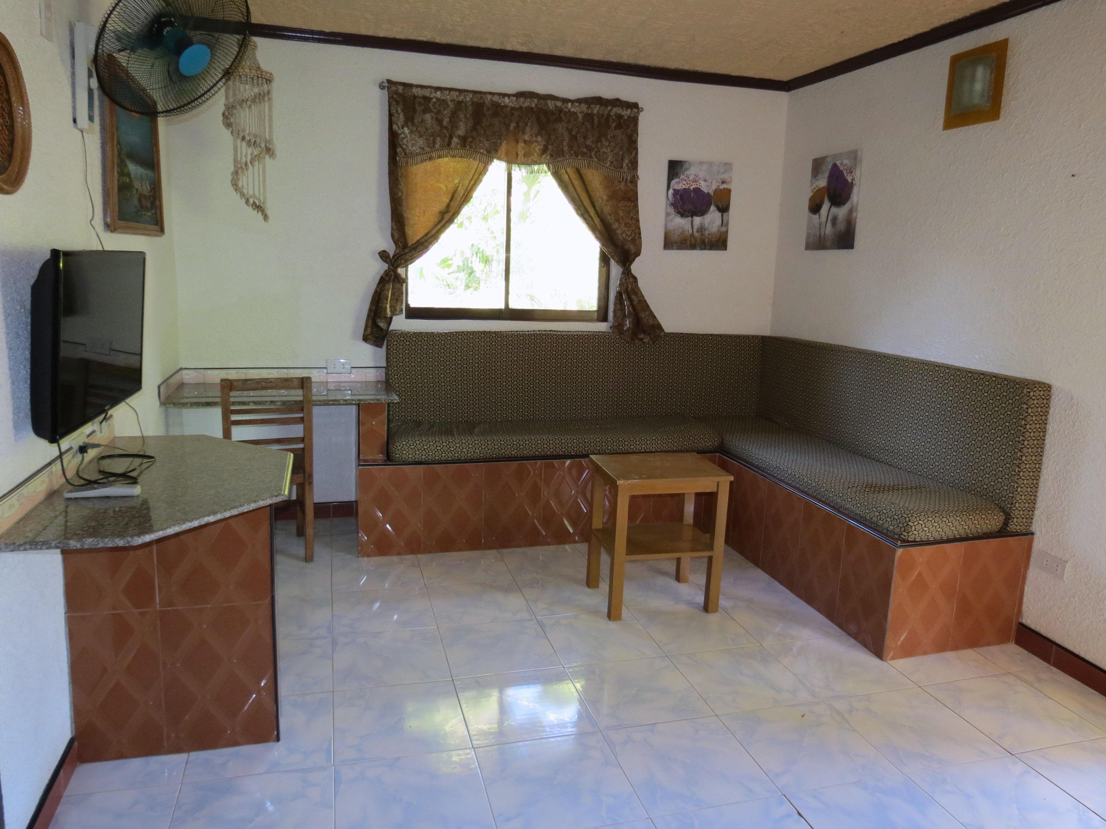 A compact living space with a kitchenette, a sofa, a small table, and a window with curtains.