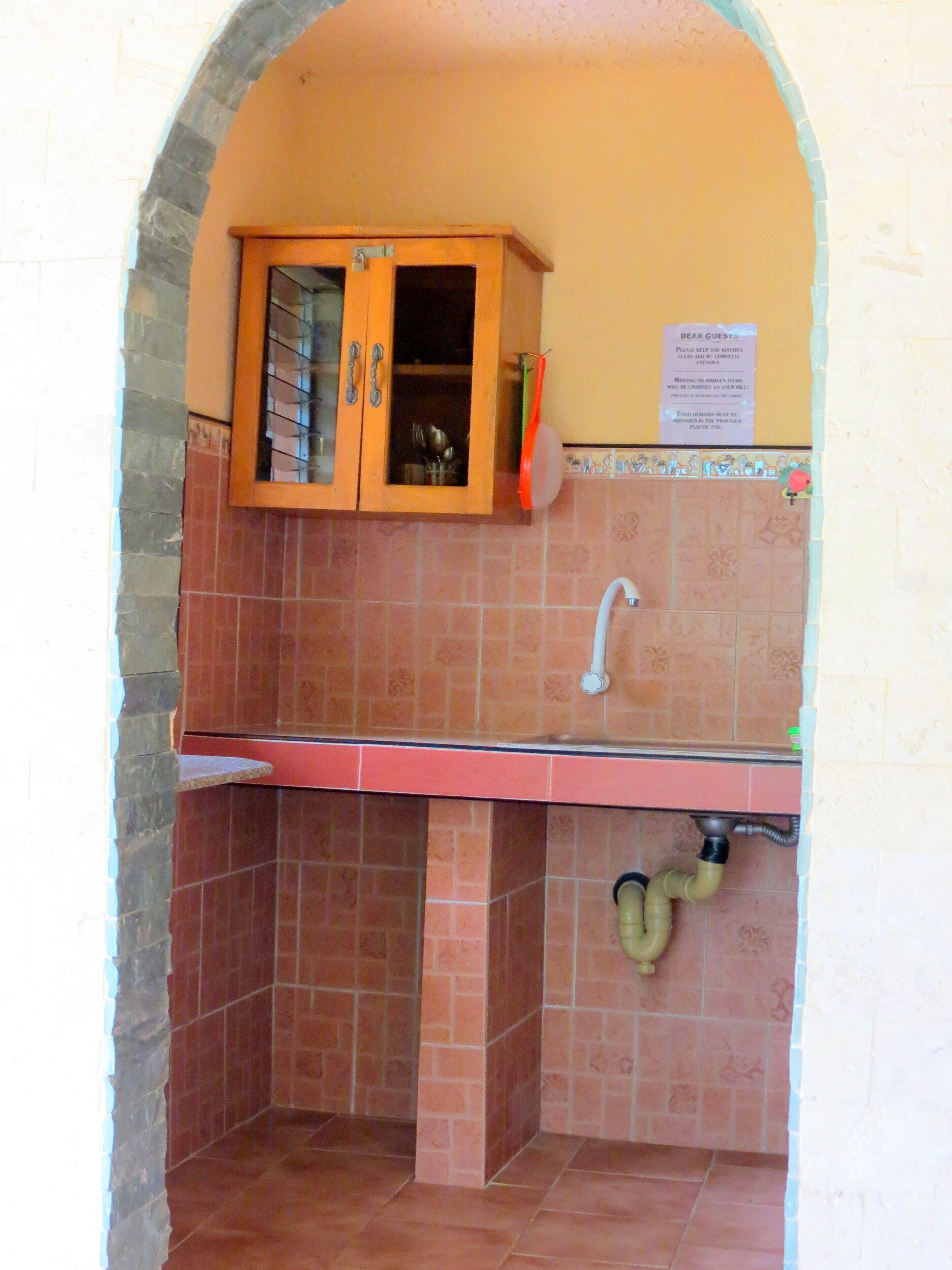 A compact kitchen with a wooden cabinet, a sink, and a tiled backsplash.