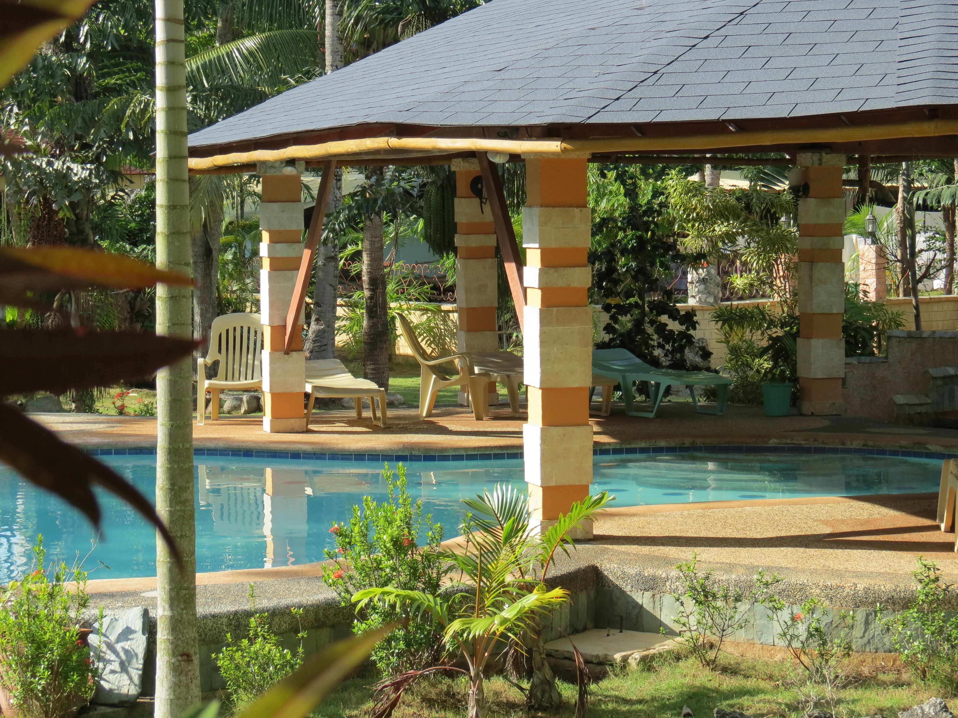 A pool area with a covered seating area, lounge chairs, and a pool.